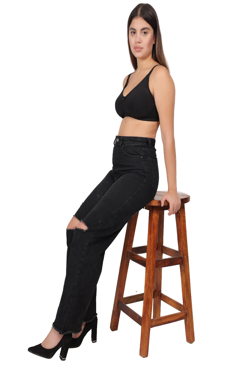 Woman wearing a black Non Padded bra and black jeans sitting on a wooden stool against a white background