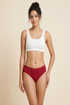 Woman wearing a white sports bra and red mid-waisted bikini bottoms on a beige background